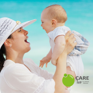 Woman in sunhat holding baby on beach with crystal blue waters in background